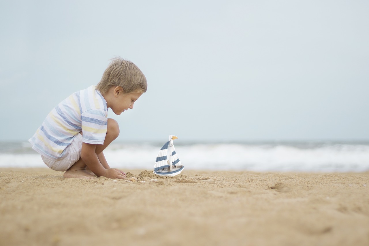 Boy playing with a sailboat on a beach.